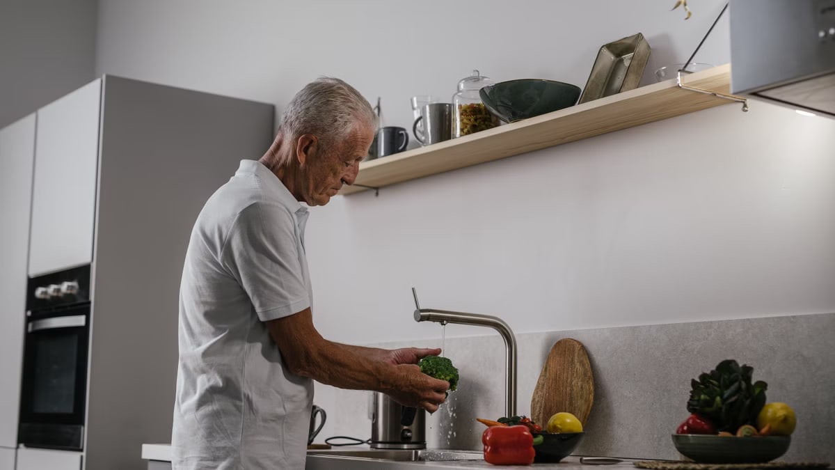 Elderly man washing fresh vegetables at a kitchen sink, depicting a healthy lifestyle.