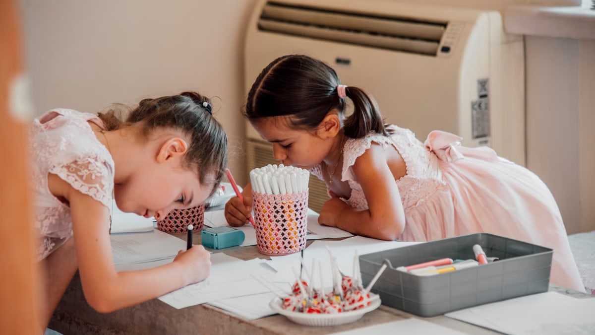 Two young girls focused on drawing with markers at a table, showcasing childhood creativity and concentration.